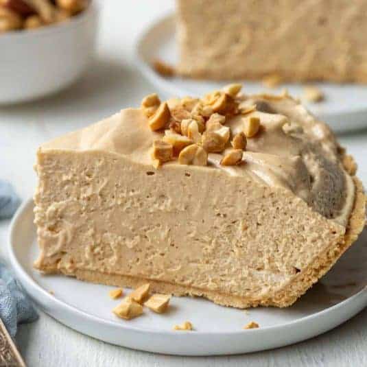 Slice of creamy peanut butter pie topped with crushed peanuts on a small white plate.