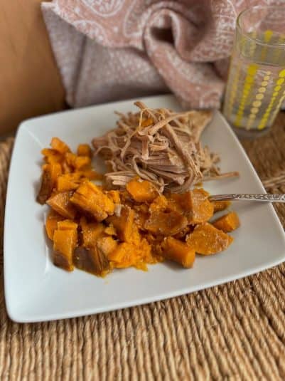 A hand holding a fork twirls spaghetti with shrimp in a white bowl, with a glass of white wine in the background on a wooden table.