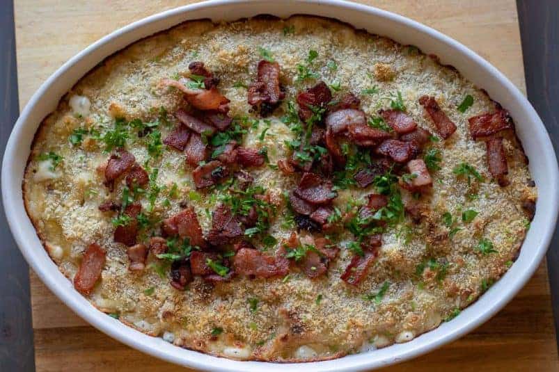 Baked Mac and cheese is garnished with crispy bacon pieces and chopped parsley.