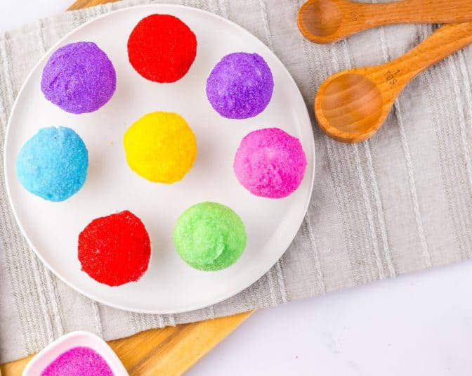 A bundt cake with white frosting and colorful sprinkles on a red plate, placed on a wooden table.