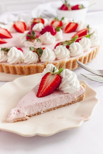 Strawberry mousse pie in the background with a slice of the pie in the front on a white plate.