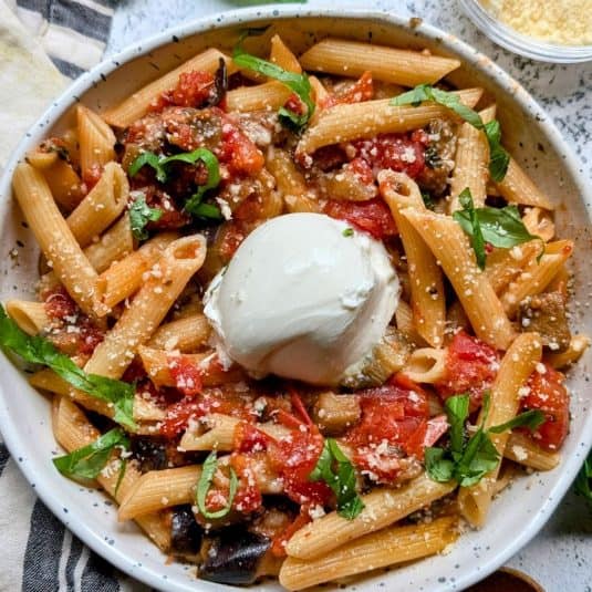 Pasta alla siciliana recipe with burrata cheese, fresh basil, and eggplant tomato sauce in a bowl.