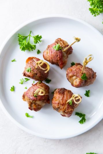 Air Fryer Bacon Wrapped Meatballs on a white plate with parsley and tooth picks.