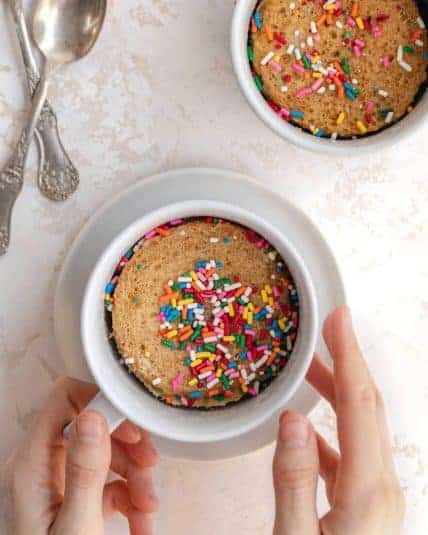 Colorful sprinkle-topped mug cakes served in white cups, ready for baking or enjoying.