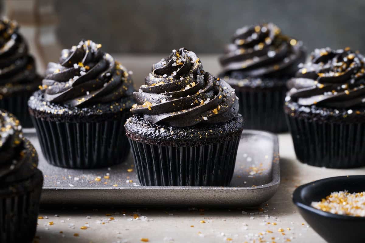 Black velvet cupcakes on a silver plate surrounded by sprinkles.