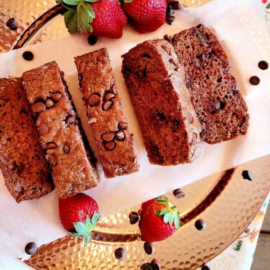 Chocolate strawberry bread sliced and presented on a serving plate with strawberries and chocolate chips.