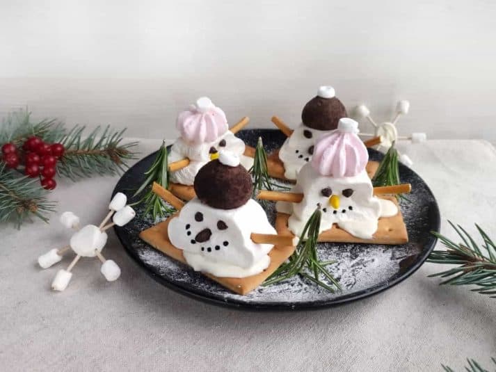 Four marshmallow snowmen on a black plate.