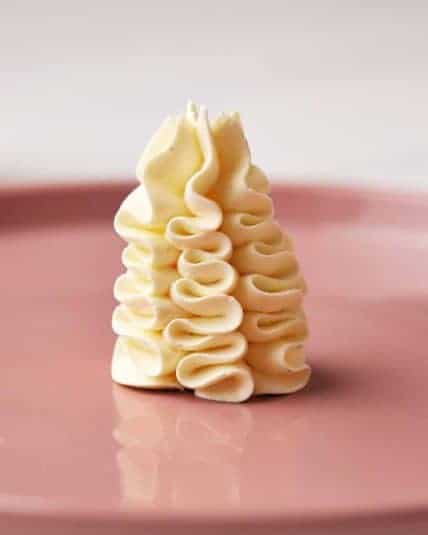 Cream cheese frosting piped in a decorative swirl on pink plate. Perfect for cakes and cupcakes.