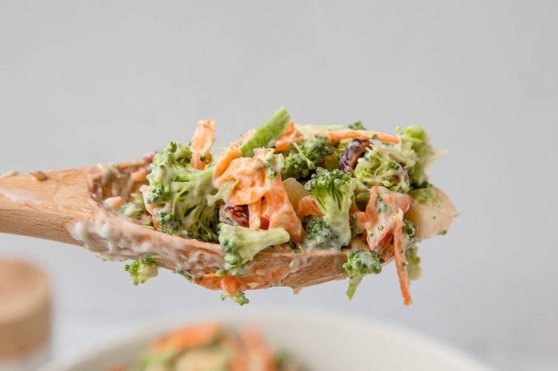 Creamy vegetable salad with broccoli, carrots, and raisins in a wooden spoon. Healthy, fresh, and delicious veggie mix.