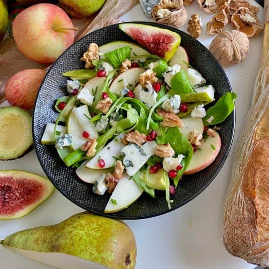 Fresh pear and blue cheese salad with walnuts and pomegranate seeds in a black bowl.