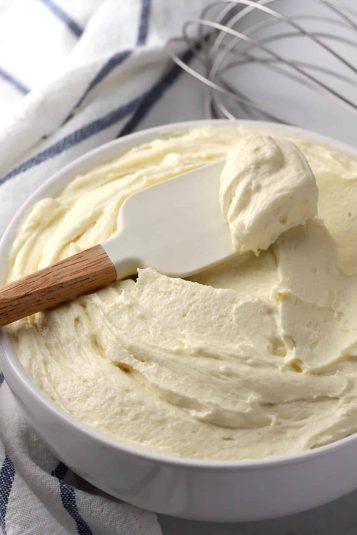 Creamy vanilla frosting in a white bowl with a spatula.
