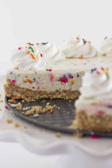 Colorful sprinkles on creamy cheesecake with a cookie crust, decorated with whipped cream and sprinkles.