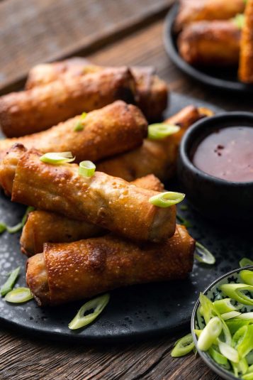 Pile of eggrolls with turkey vegetable filling on black plate.