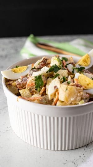 Creamy potato salad with hard-boiled eggs, herbs, and bacon in a white ramekin for summer gatherings.