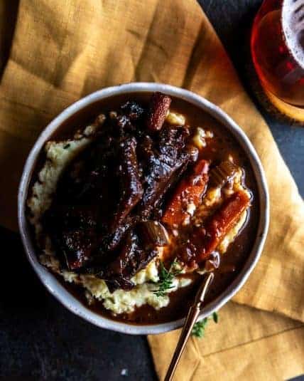 Overhead view of tender slow cooker short ribs with carrots and sauce served over mashed potatoes in a bowl.