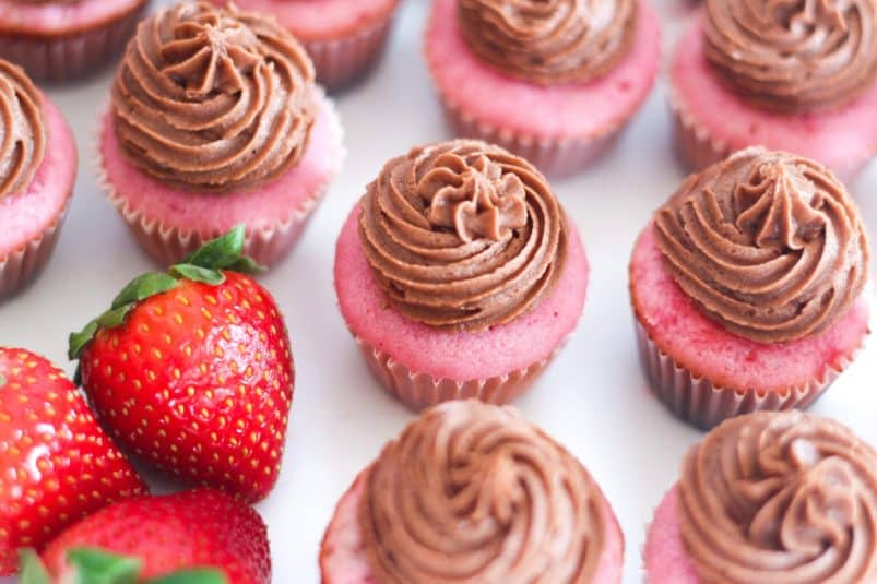 Pink bite-sized strawberries and champagne cupcakes with nutella buttercream next to a couple strawberries.