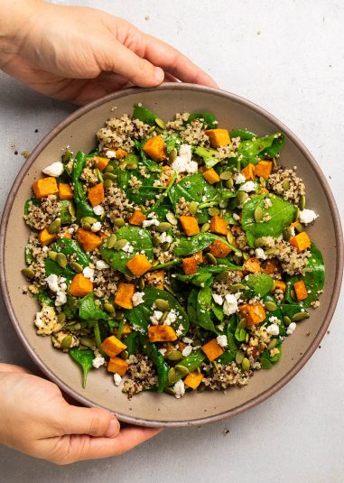 Fresh quinoa spinach salad with roasted sweet potatoes and feta cheese, healthy vegan side dish.