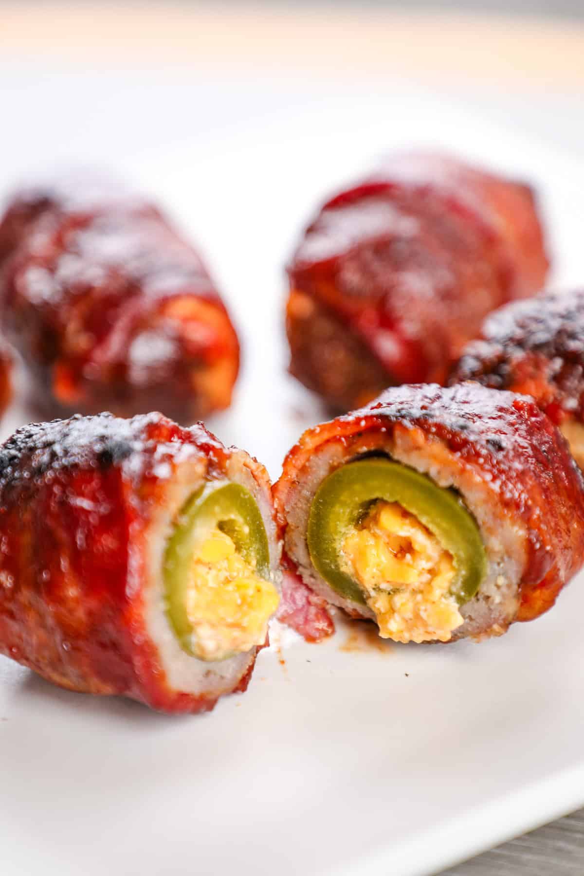 Crispy bacon-wrapped jalapeño poppers with creamy cheese filling on a white plate.