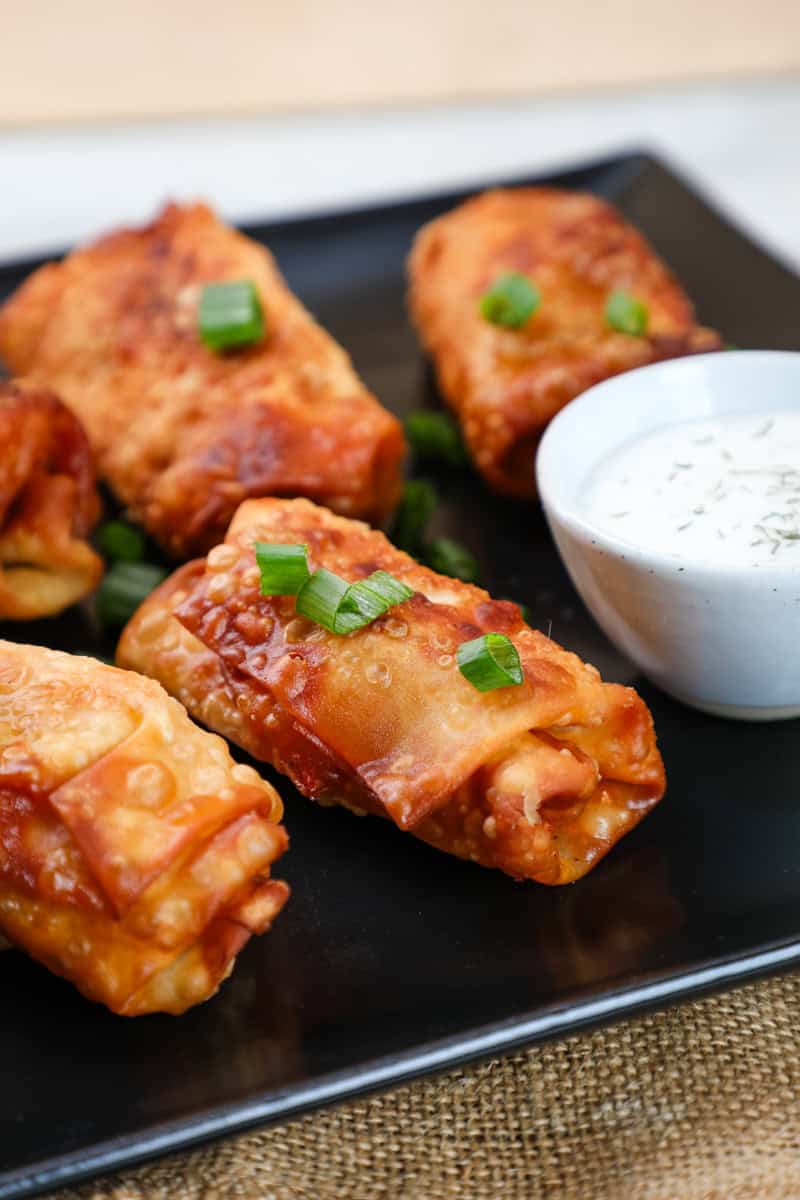 a plate of buffalo chicken dip egg rolls garnished with green onions.