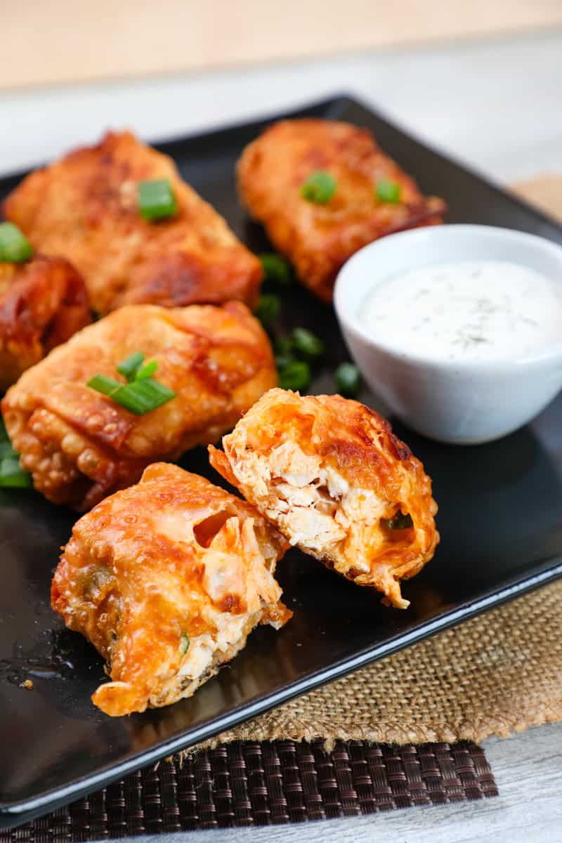 a buffalo chicken egg roll with cheese cut in half with ranch dip in the background.