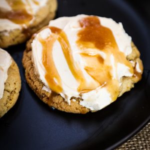 Butterscotch cookie with whipped cream and caramel sauce on black plate.