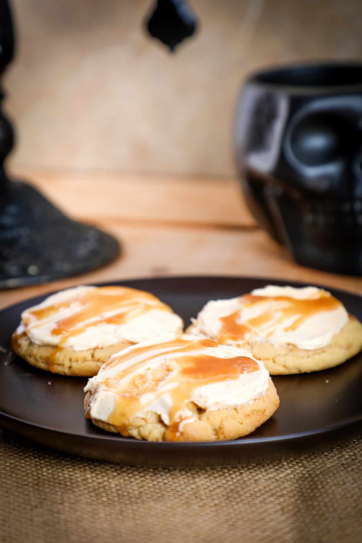 Fluffy sugar cookies with cream cheese frosting and caramel drizzle on a black plate.
