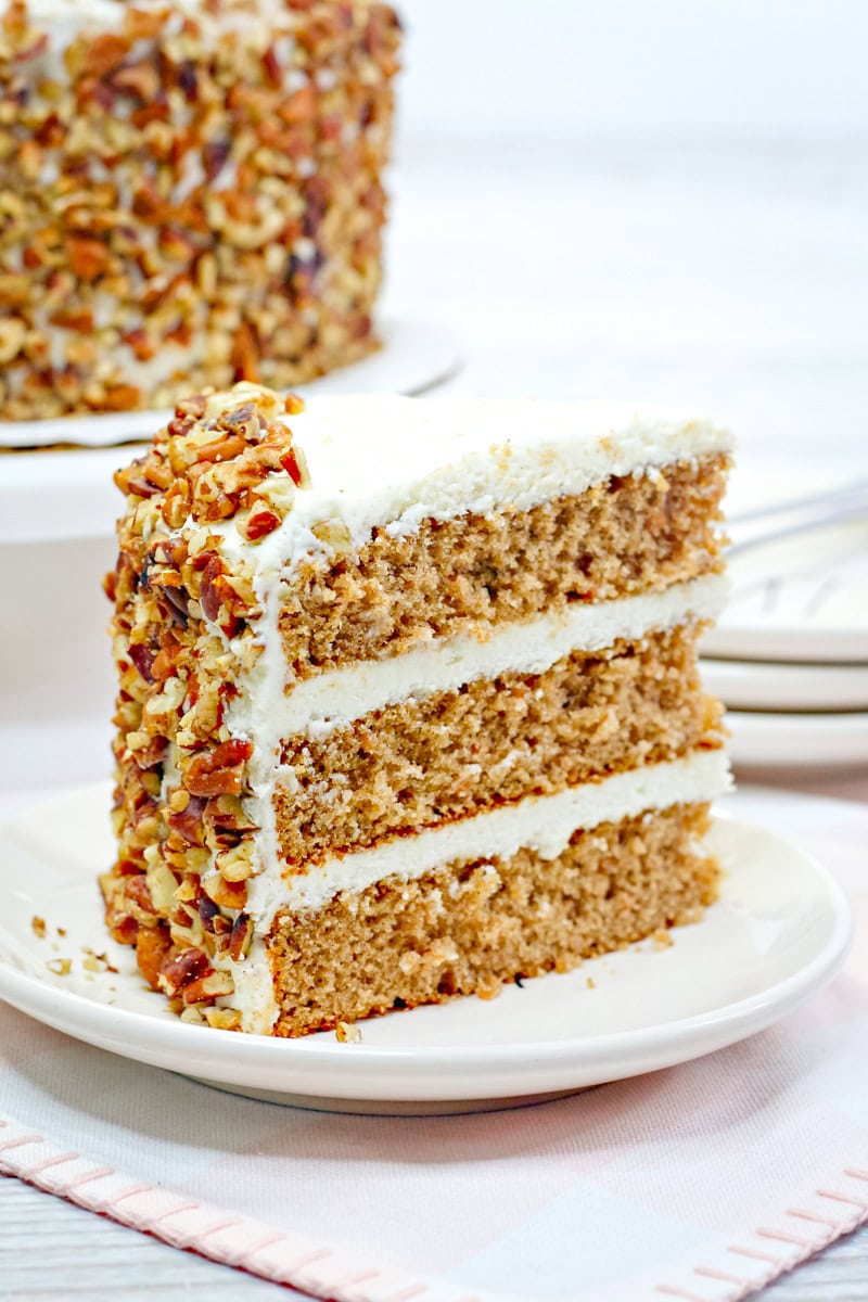 a 3 layer slice of carrot cake with cream cheese frosting and decorated with chopped pecans. 