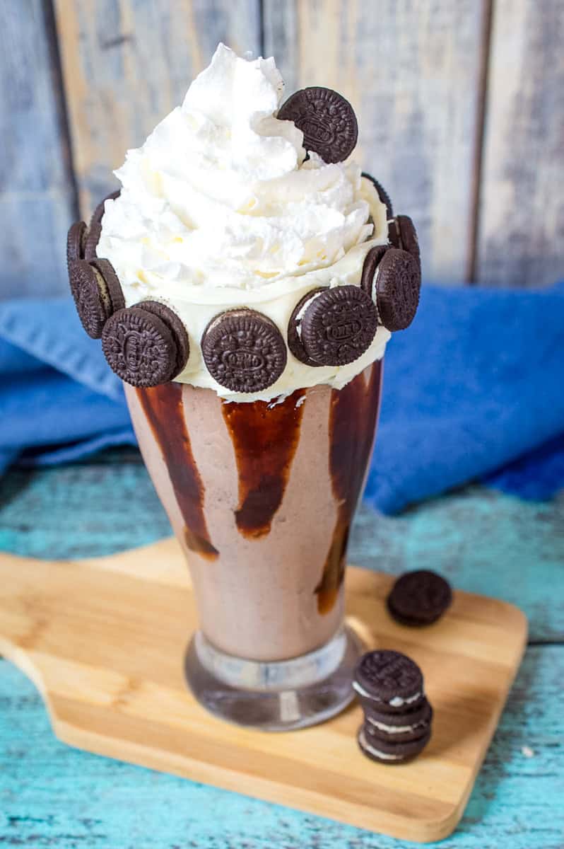 a chocolate oreo milkshake with chocolate syrup, whipped cream, and frosting with mini Oreos.