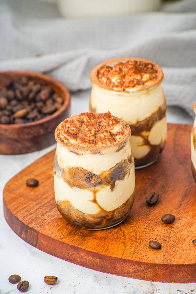 two tiramisu desserts in a jar topped with mascarpone whipped cream and cocoa powder. 