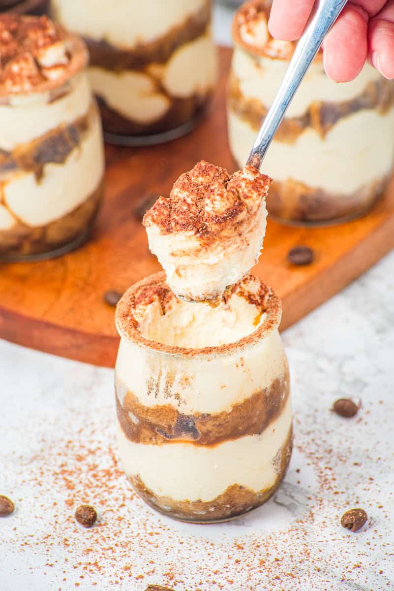 a spoon lifting out ladyfingers topped with mascarpone cream and cocoa powdered from a tiramisu dessert cup.
