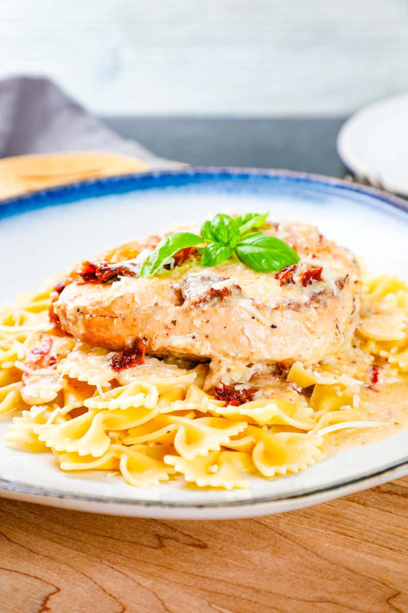 slow cooker marry me chicken with sun dried tomatoes on top of farfalle pasta and garnished with basil.