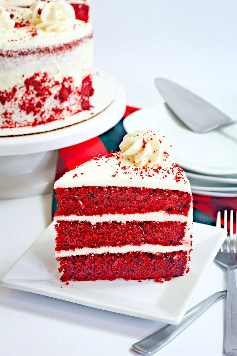 a 3 layer slice of red velvet cake with cream cheese frosting and cake crumbs.