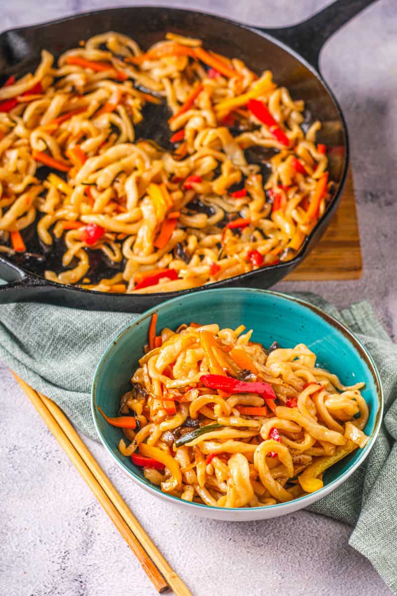 a bowl of vegan Yaki Udon with peppers, mushrooms, and carrots in a sweet and spicy sauce.