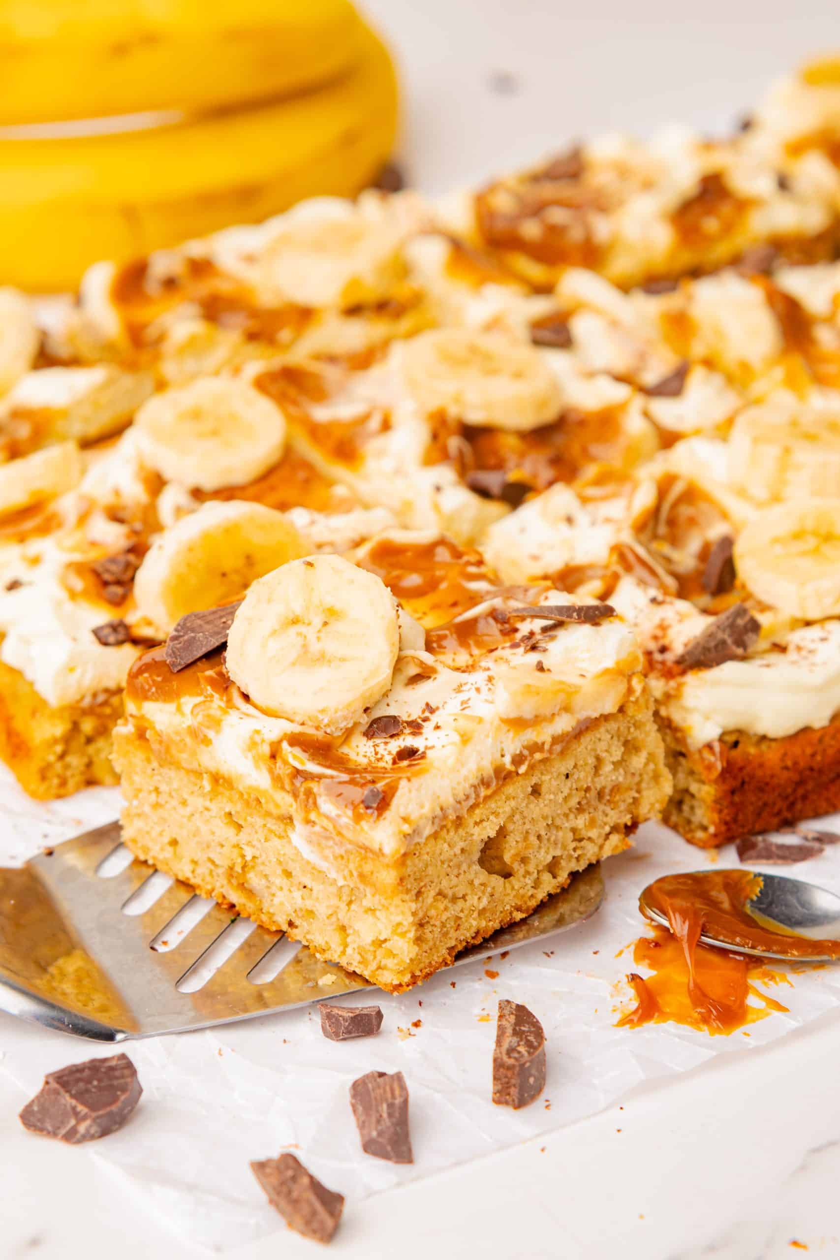 a slice of banoffee cake topped with dulce de leche, whipped cream, sliced bananas, and chocolate. 
