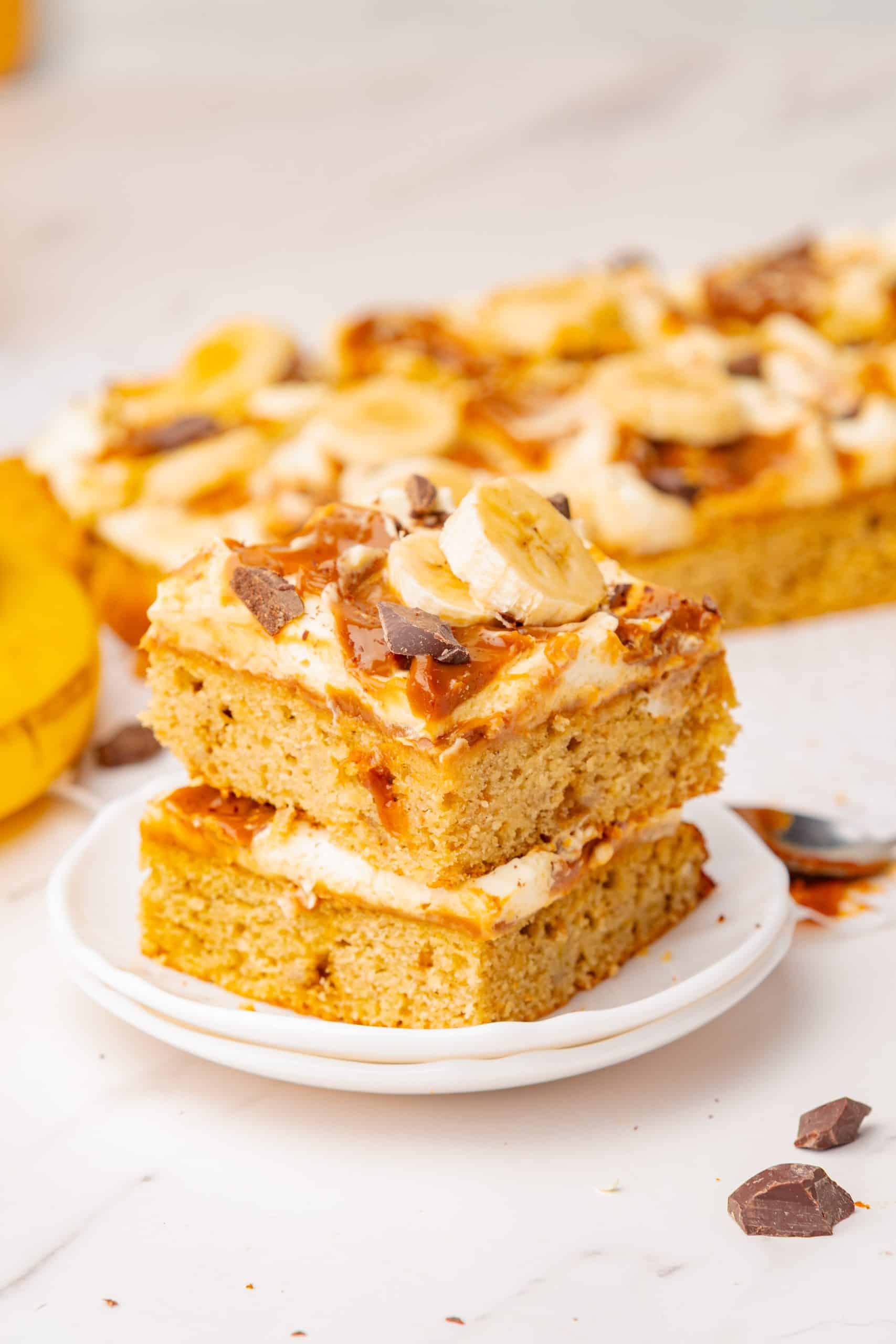 two slices of banana cake on top of each other topped with bananas, chocolate, dulce de leche, and whipped cream.