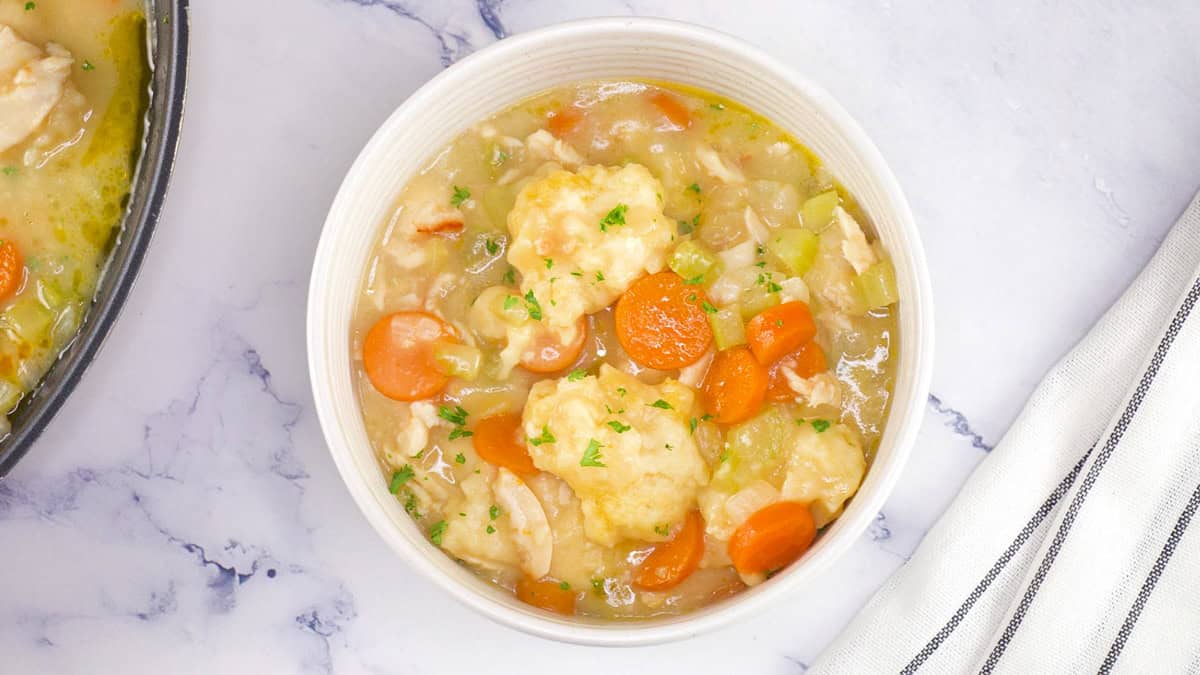 a bowl of chicken and dumplings with carrots and onions garnished with parsley.