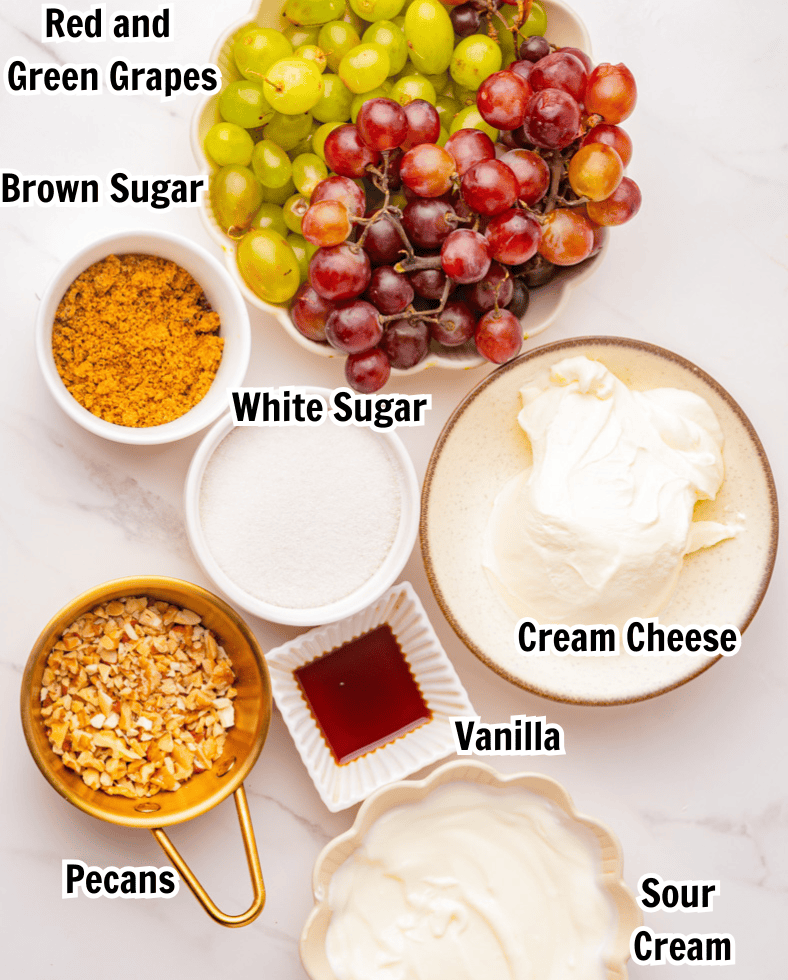 ingredients in bowls including red and green grapes, sugar, cream cheese, brown sugar, pecans, and sour cream.