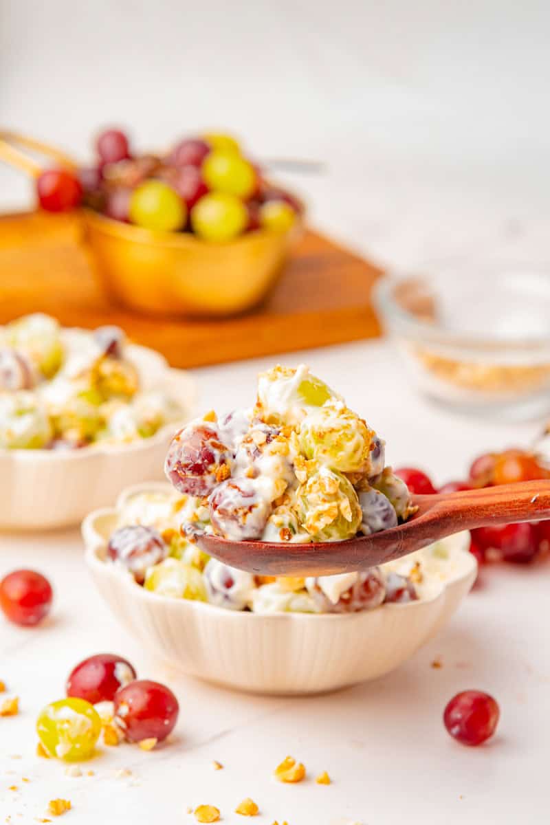 a spoon lifting out a serving of cream cheese grape salad topped with nuts and brown sugar.