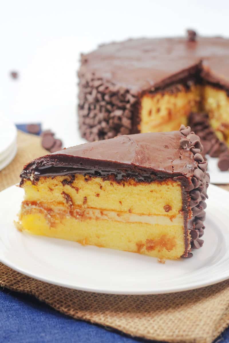 a slice of boston cream cake with a pastry cream filling, chocolate ganache, and mini chocolate chips.