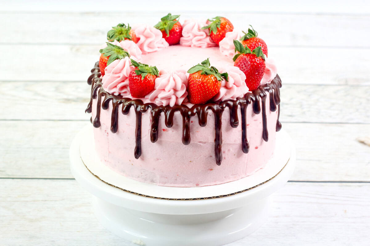 a chocolate cake with strawberry buttercream and a chocolate drip topped with piped frosting and fresh strawberries.