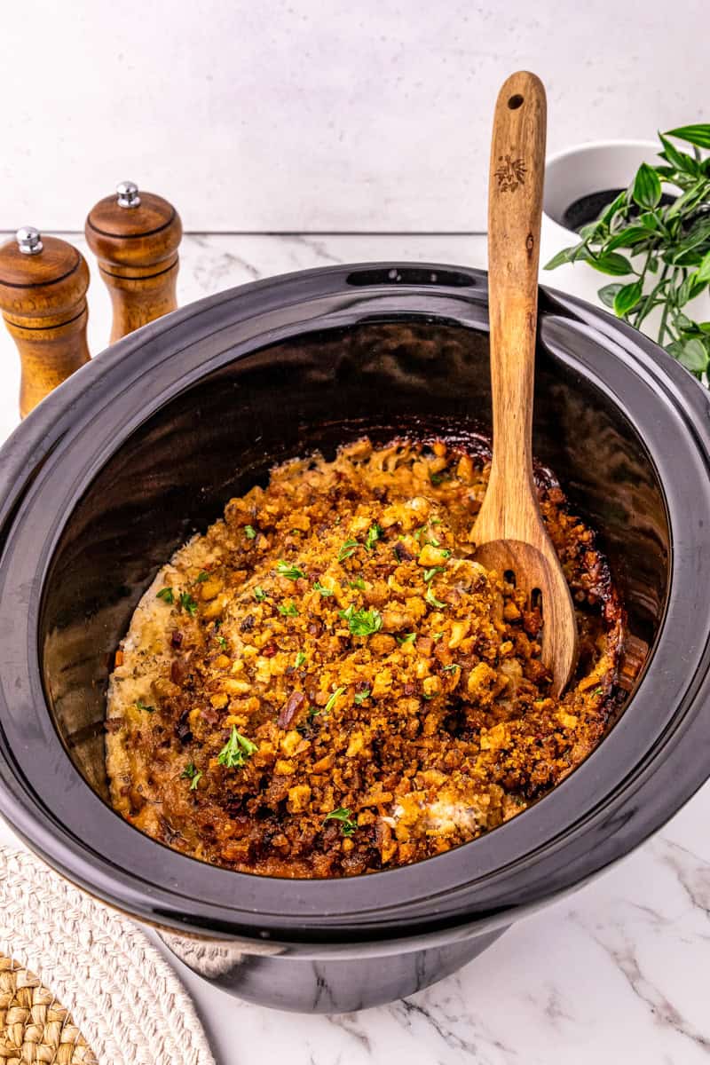 a black slow cooker with pork chops topped with stuffing.