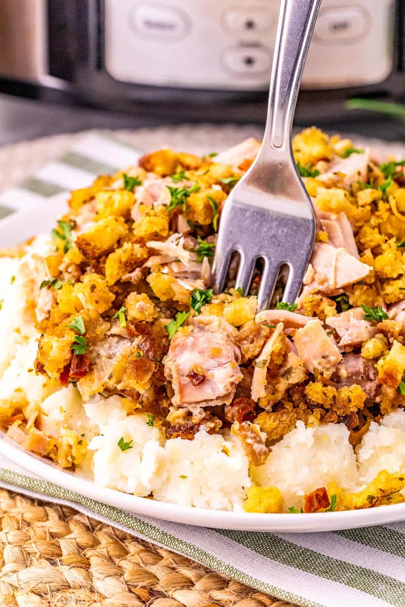 a fork inside pork and stuffing from the slow cooker on top of mashed potatoes.