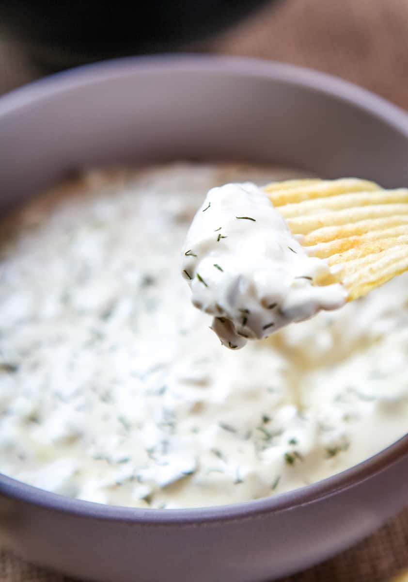 a ruffled potato chip with dill pickle dip on it with a dill garnish.