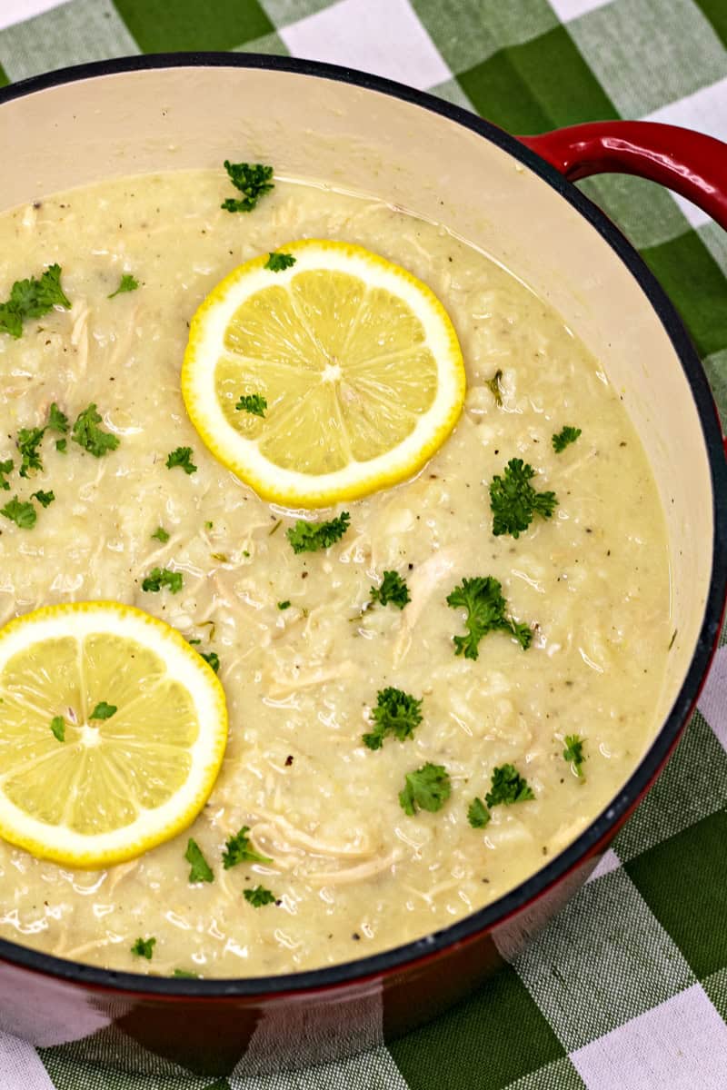 a Dutch oven of Greek lemon chicken soup with rice garnished with parsley and lemon slices.