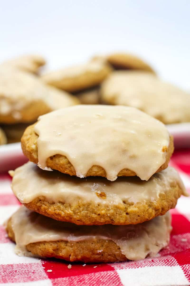 3 soft iced oatmeal cookies topped with a vanilla glaze on a red checkered tablecloth.
