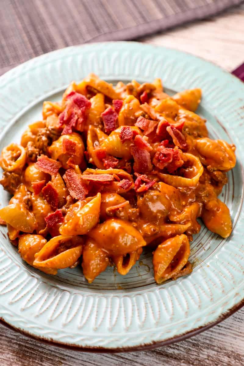 a plate of bacon cheese burger pasta with shell pasta and a creamy tomato cheese sauce garnished with bacon.