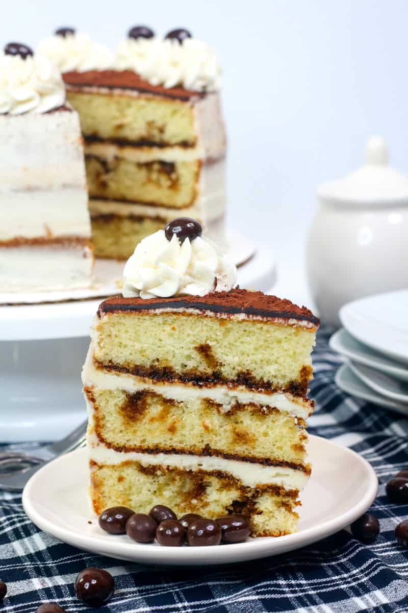 a slice of tiramisu cake with coffee soaked vanilla cake, mascarpone frosting and a cocoa powder garnish.