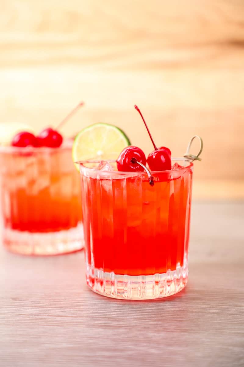a cherry bomb cocktail garnished with a lime slice and maraschino cherries.