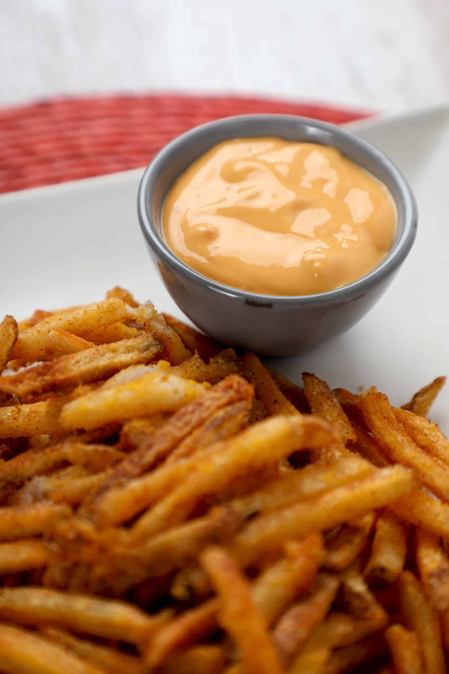copycat taco bell nacho cheese sauce in a metal container on a plate with nacho fries.