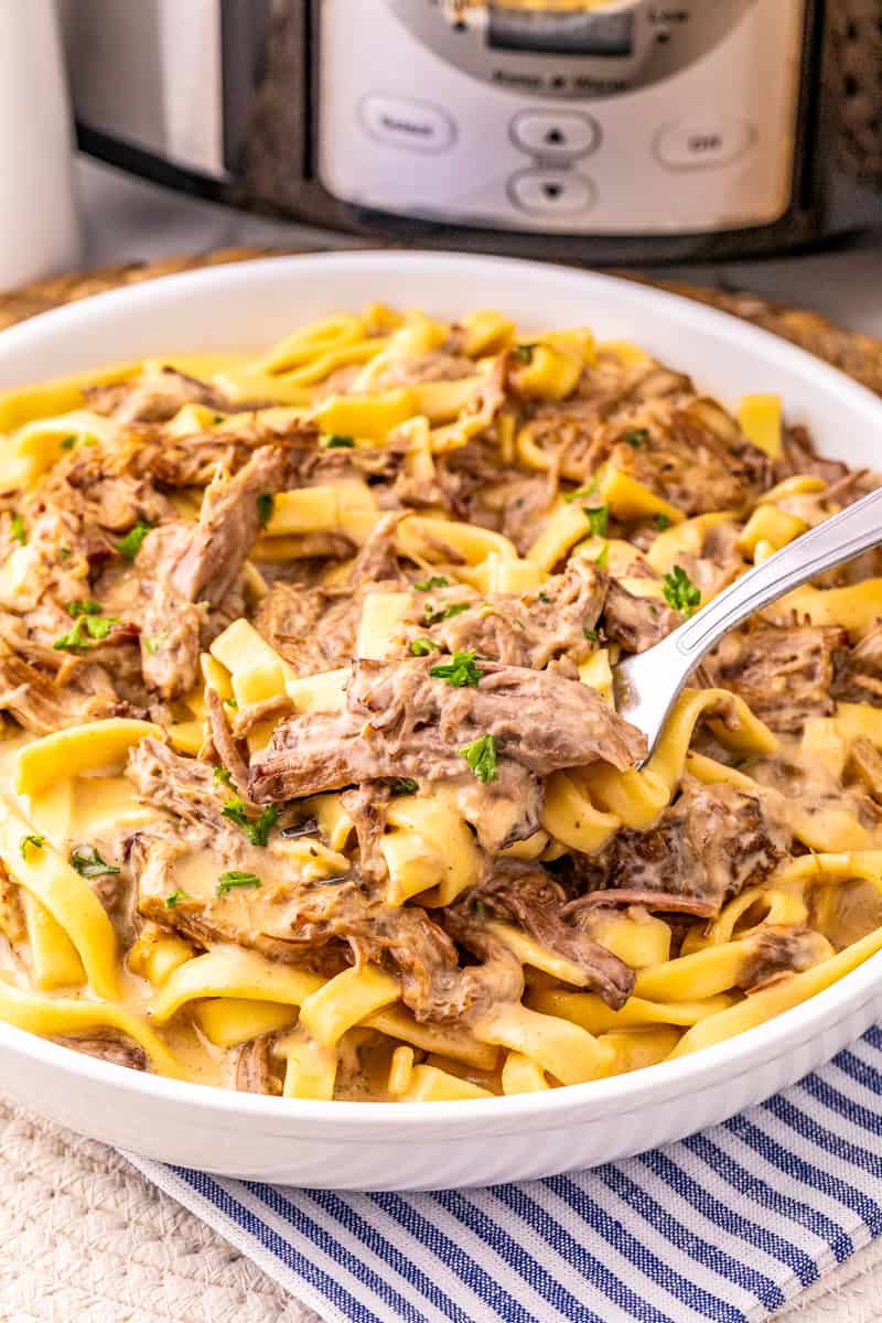 a fork with crock pot shredded beef roast and fettuccine egg noodles in a creamy gravy.